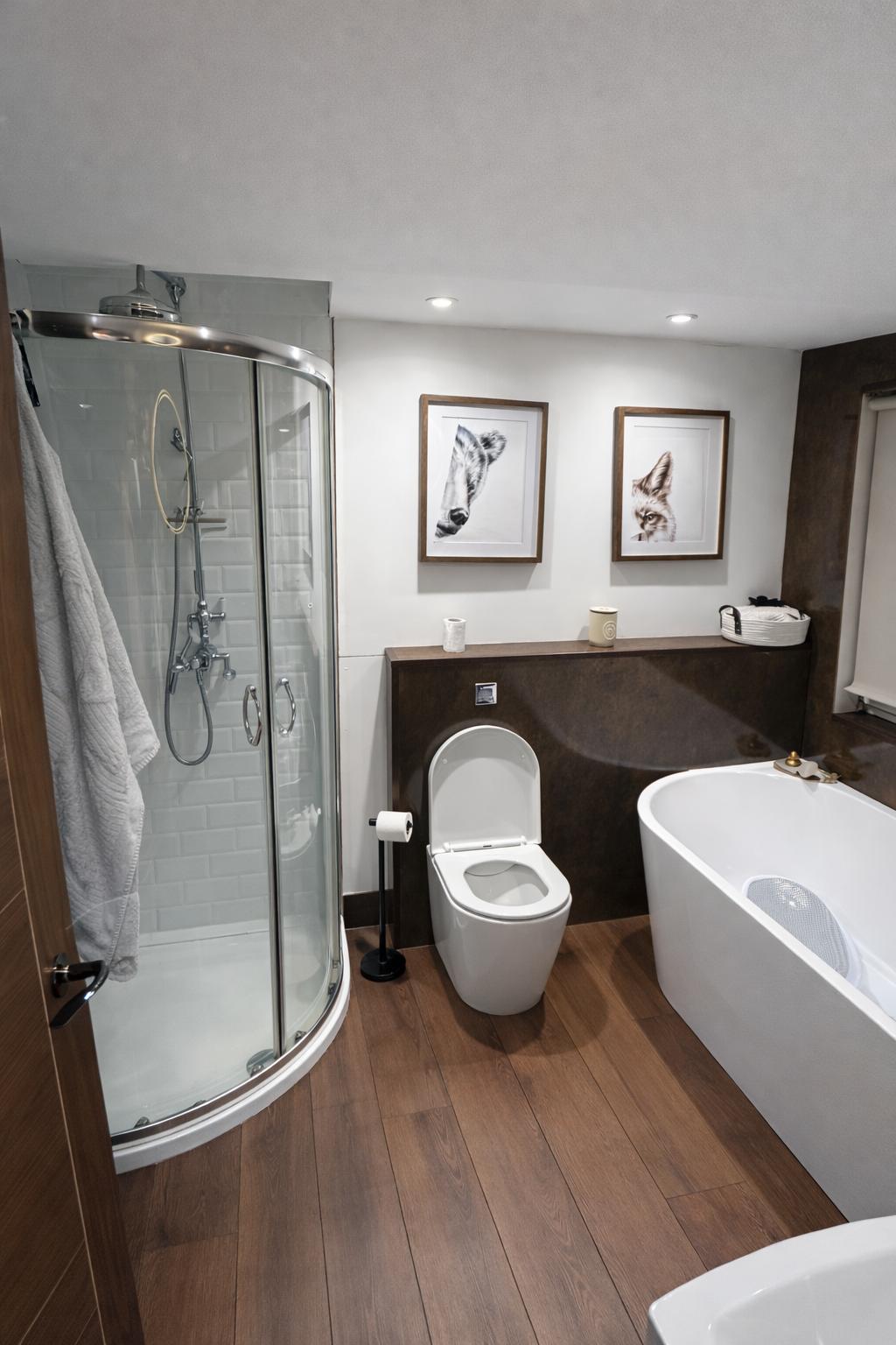 Finished luxury cabin bathroom with curved shower enclosure, freestanding bath, wood flooring and dark wall panels