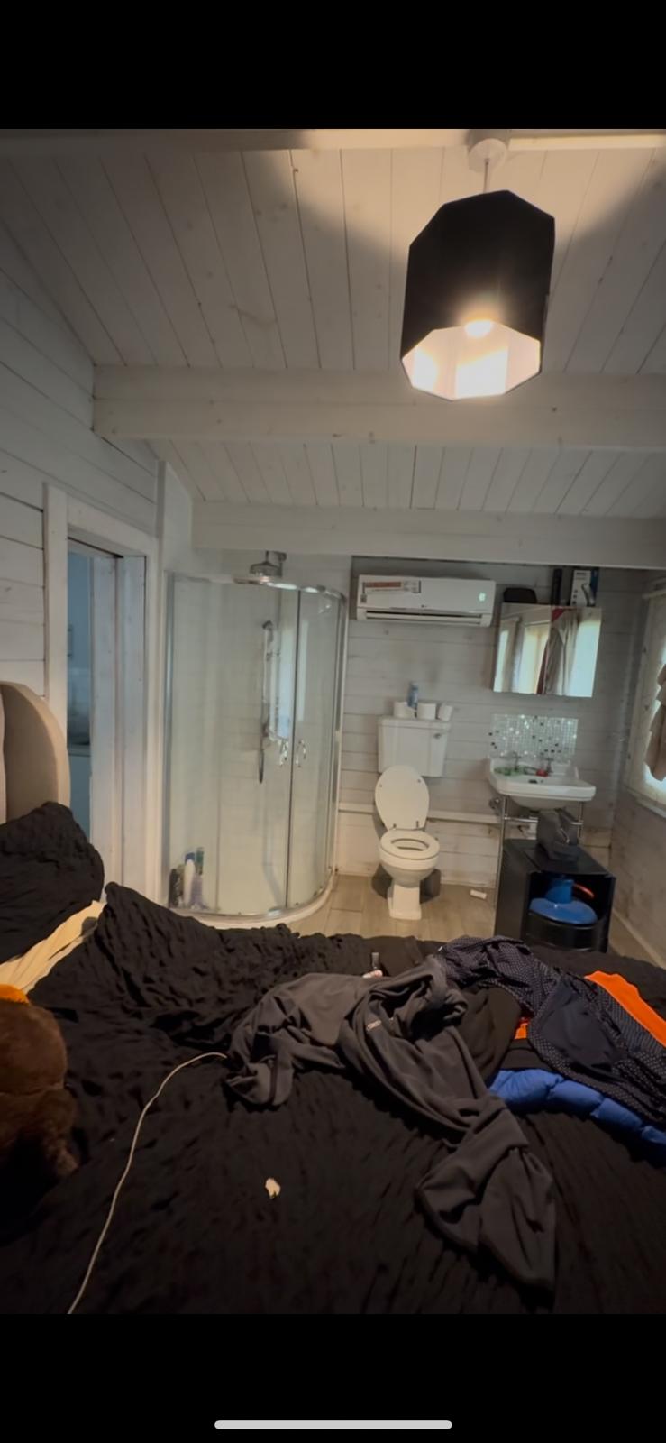Basic cabin en-suite with corner shower, toilet and white timber walls before renovation