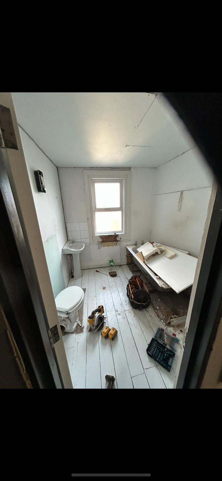 Bathroom stripped back with old fixtures, exposed floorboards and tools before renovation
