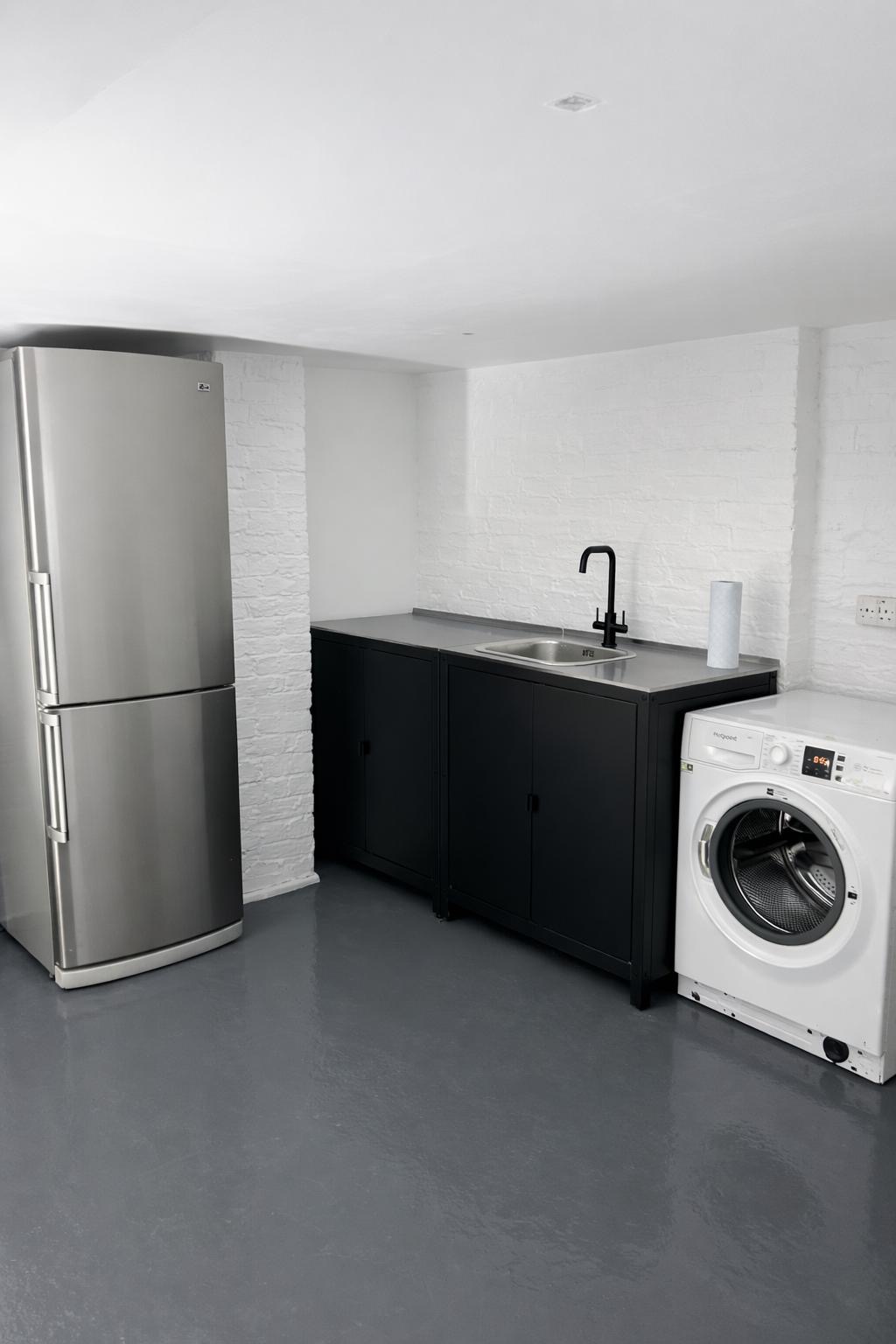 Modern utility room with black cabinets, washing machine and epoxy floor